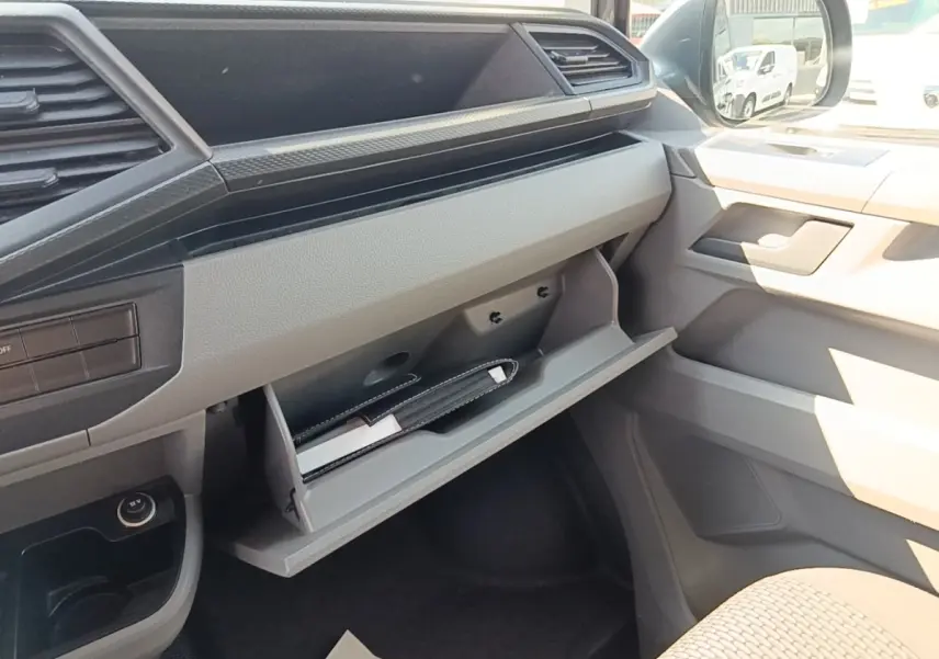 Intérieur côté passager du Volkswagen Transporter gris foncé 2022, avec boîte à gants ouverte et tableau de bord clair.