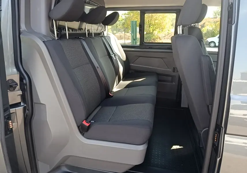 Vue intérieure côté gauche du Volkswagen Transporter gris foncé, montrant la banquette arrière trois places et la cloison vitrée.