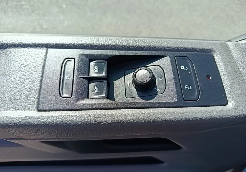 Gros plan sur les commandes de réglage des rétroviseurs et des vitres électriques côté conducteur du Volkswagen Transporter gris foncé.