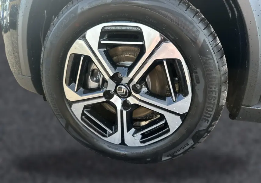 Gros plan sur la jante alu noire et argentée d'une Citroën C3 Aircross noire, mettant en valeur le logo central.