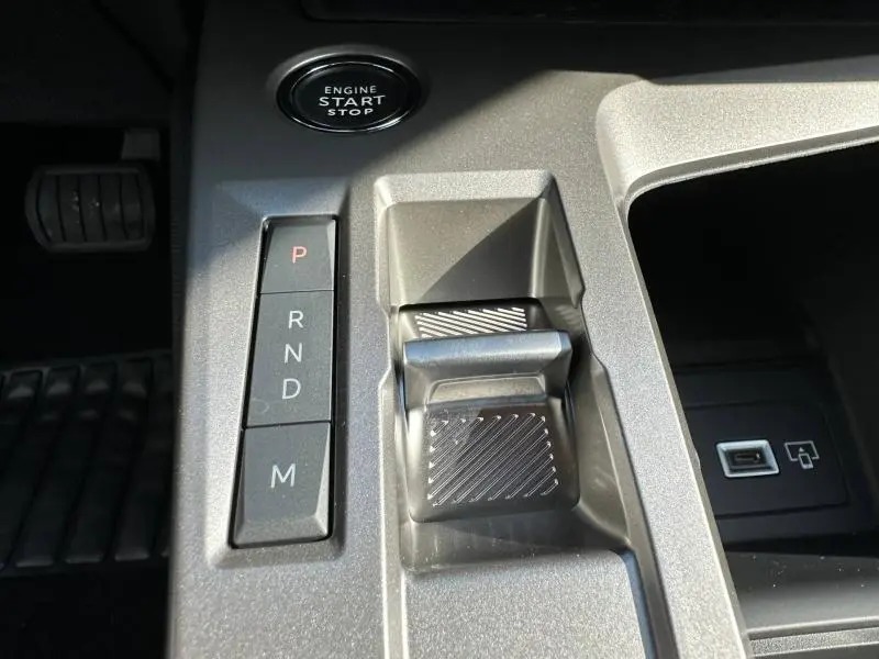 Gros plan sur la console centrale grise de la Peugeot 308 2025, montrant le levier de boîte auto et le bouton start/stop.
