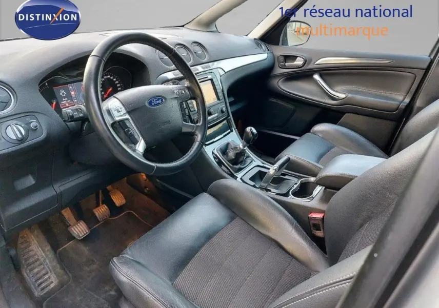 Intérieur du Ford S-MAX 2012 vu côté conducteur, volant cuir noir, tableau de bord avec écran GPS et boîte manuelle.