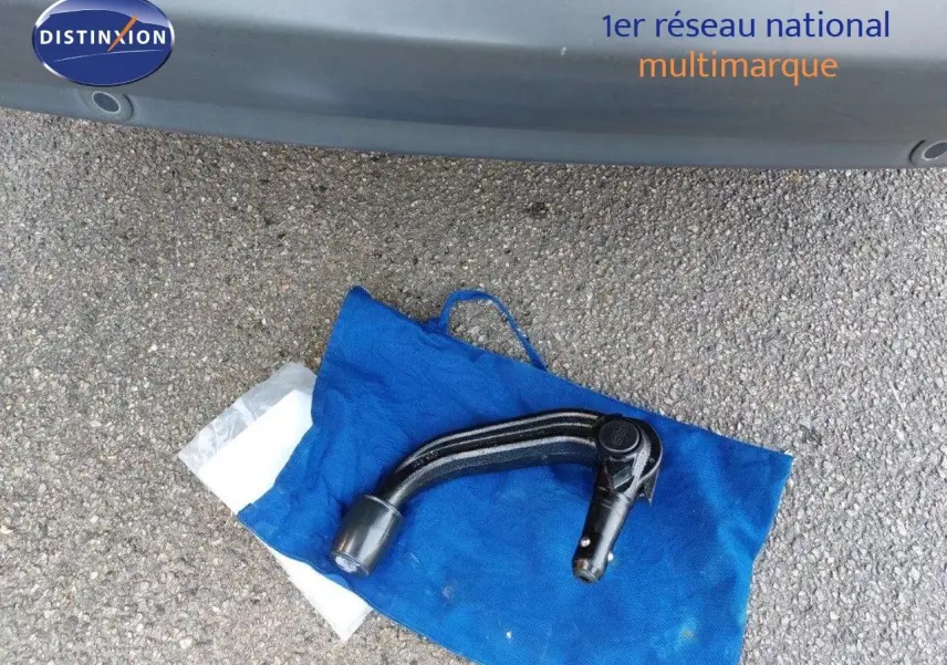 Gros plan sur l'attelage noir posé sur un sac bleu devant un Ford S-MAX gris clair métal, vue arrière basse.