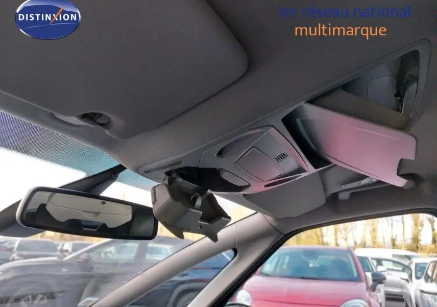 Vue intérieure du pare-soleil et du rétroviseur d'une Ford S-MAX gris clair, avec un parking en arrière-plan.