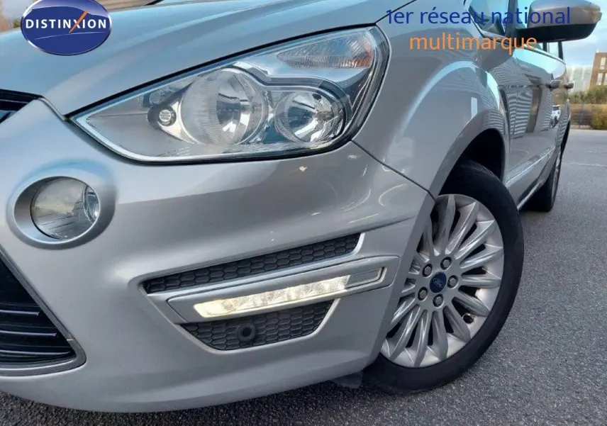 Gros plan sur l'avant droit gris clair métallisé d'une Ford S-MAX 2012 avec phare et jante alliage visible.