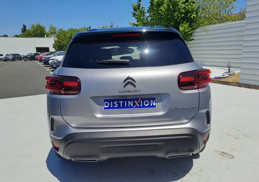 Vue arrière d'un Citroën C5 Aircross gris Artense avec toit noir, immatriculé Distinxion, en extérieur lumineux.