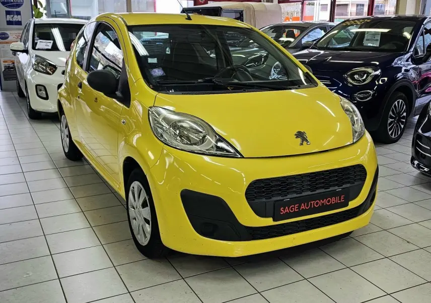 Vue 3/4 avant d'une Peugeot 107 jaune vif en showroom, avec calandre noire et logo lion visible sur le capot.