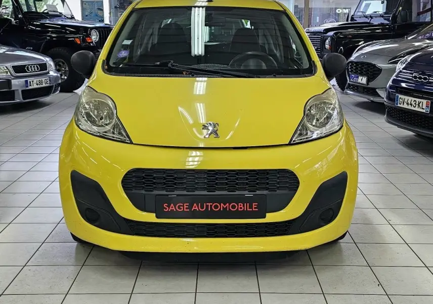 Vue frontale d'une Peugeot 107 jaune vif exposée en showroom avec calandre noire et logo lion visible.