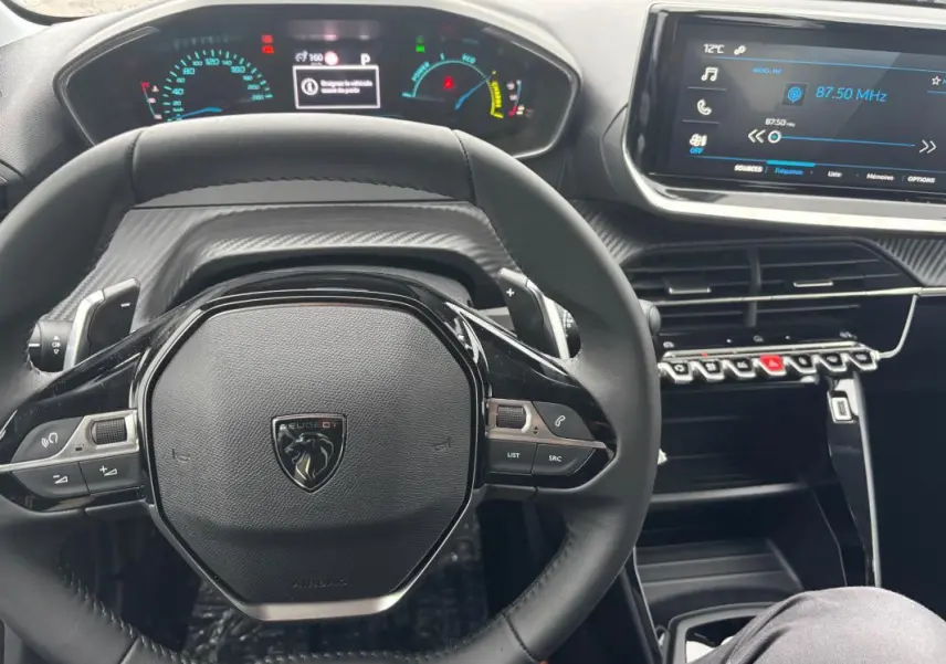 Vue rapprochée du volant noir et du cockpit numérique de la Peugeot 208 Hybrid 100 e-DCS6 Style gris 2025.