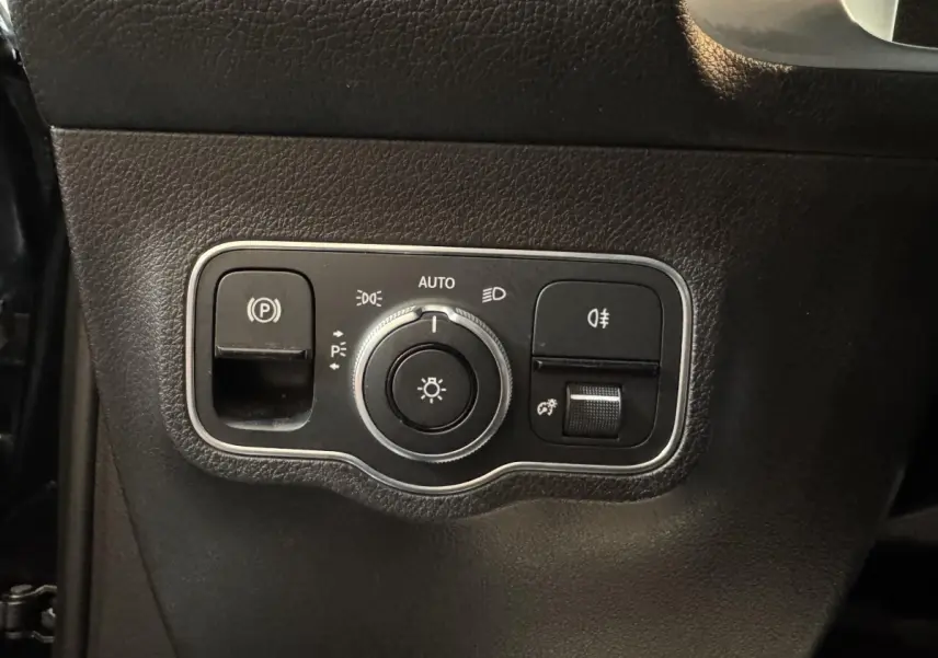 Gros plan sur le panneau de commande des phares et du frein à main électrique dans un Mercedes GLB 200 d AMG Line noir.