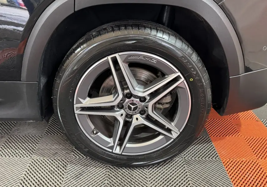 Gros plan sur la roue avant droite noire du Mercedes GLB 200 d AMG Line avec jante AMG à cinq branches.