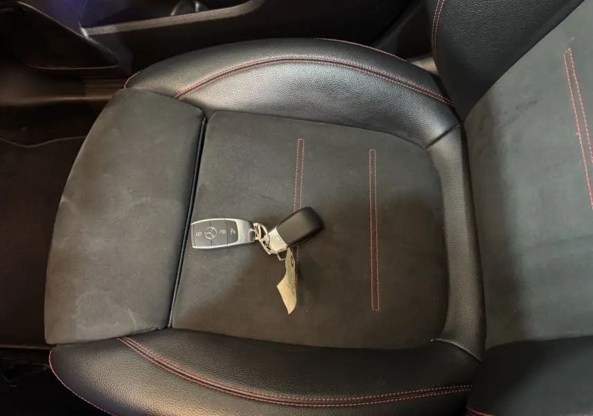 Gros plan sur la clé Mercedes posée sur un siège avant en cuir noir avec surpiqûres rouges du GLB 200 d AMG Line.