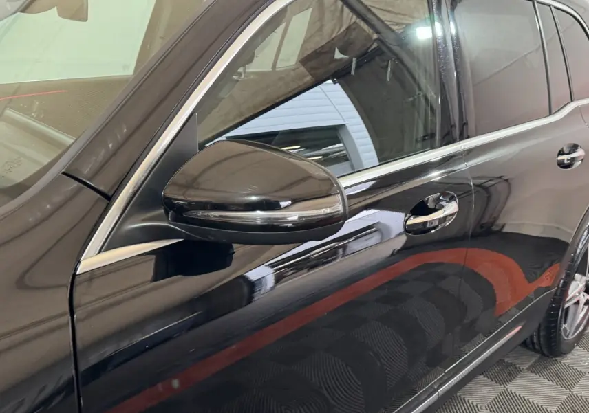 Vue latérale côté gauche sur la porte avant et rétroviseur d’un Mercedes GLB 200 d AMG Line noir brillant.