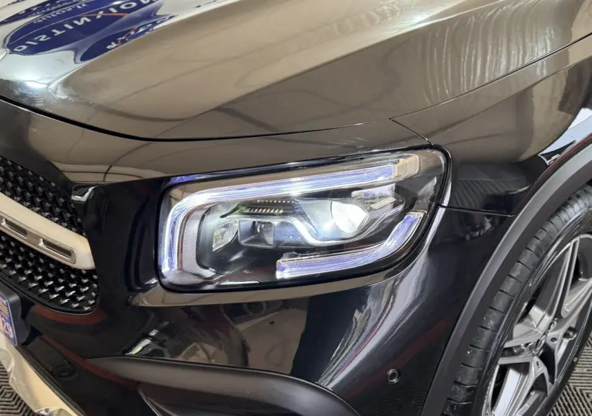 Gros plan sur le phare avant droit du Mercedes GLB 200 d AMG Line noir, avec jante alliage visible et calandre partielle.