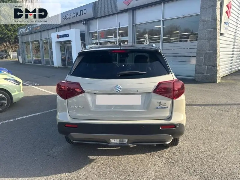 Vue arrière d'un Suzuki Vitara 1.4 Boosterjet Hybrid 2026 en So'Color Savanna Ivory/Black métal, avec toit noir et feux rouges.