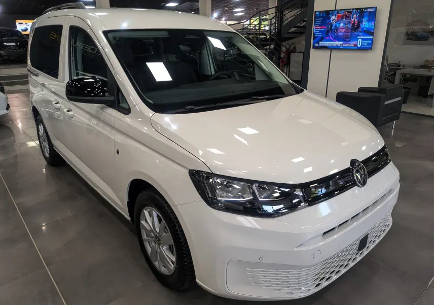 Vue 3/4 avant droite d'un Volkswagen Caddy blanc 2025 en showroom avec calandre noire et phares LED.