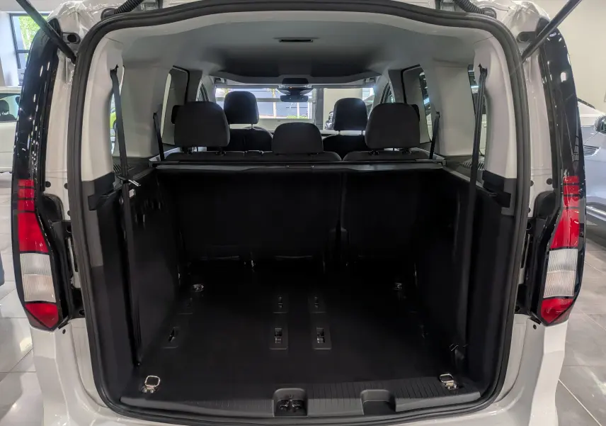 Vue arrière ouverte du coffre spacieux d'un Volkswagen Caddy blanc 2025, montrant les sièges arrière et l'espace de chargement.