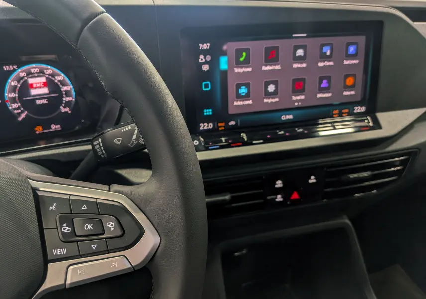Vue intérieure du tableau de bord du Volkswagen Caddy 2025, avec volant à commandes et écran tactile central allumé.