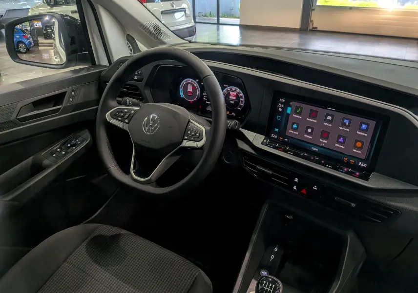 Vue intérieure côté conducteur du Volkswagen Caddy 2025, tableau de bord numérique et écran tactile couleur, volant multifonction noir.
