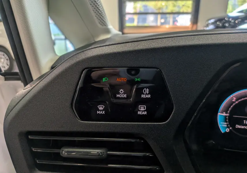 Gros plan sur le tableau de bord noir du Volkswagen Caddy blanc, montrant les commandes d’éclairage et de désembuage côté gauche.