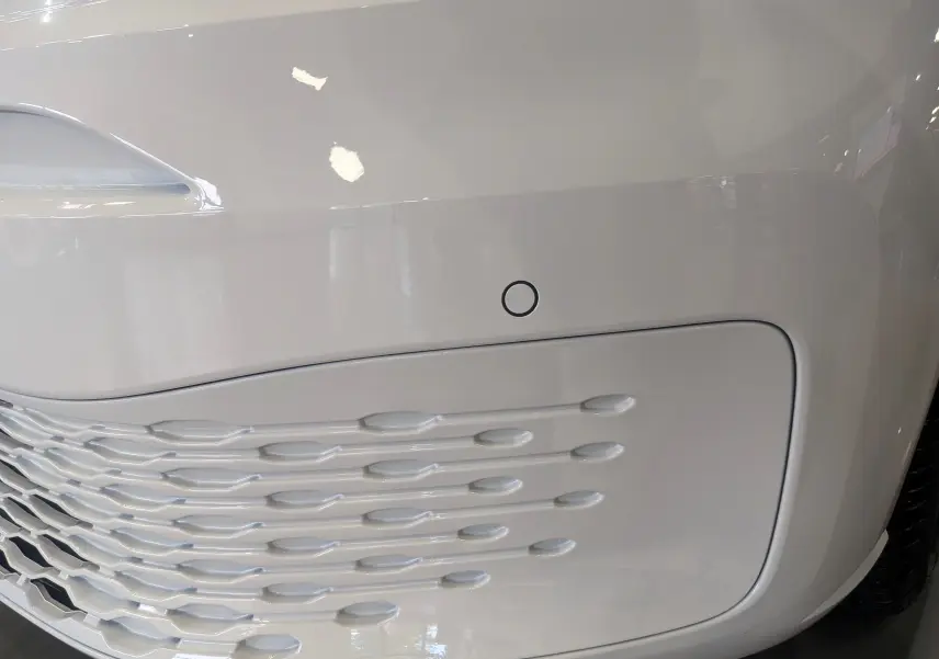 Gros plan sur la partie avant droite blanche du Volkswagen Caddy 2.0 TDI 102 ch avec capteur de stationnement intégré.