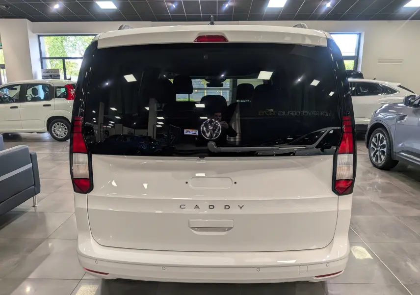 Vue arrière du Volkswagen Caddy blanc 2025 avec vitres arrière teintées et logo VW bien visible en concession.