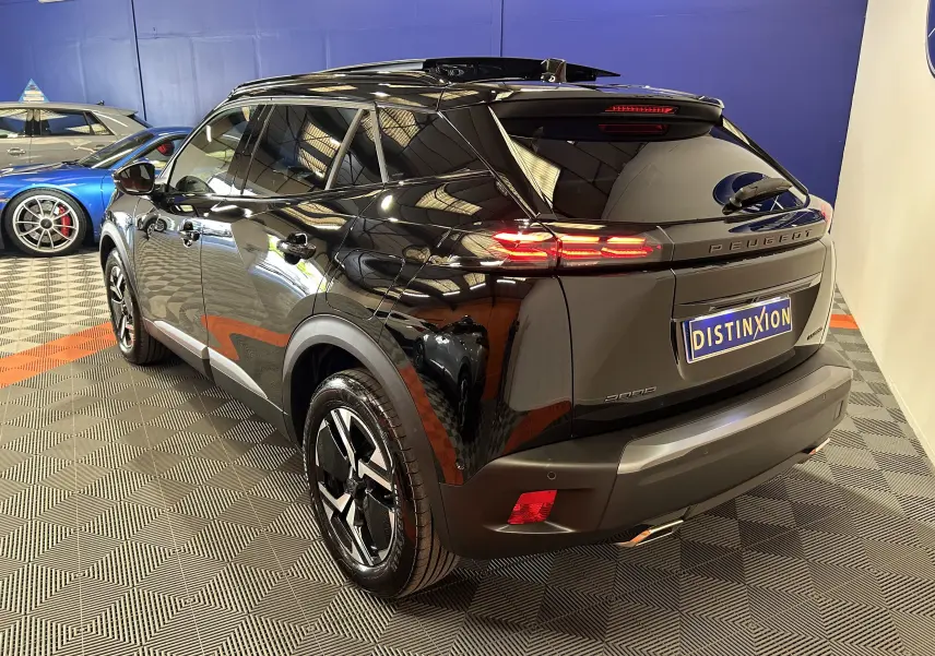Vue 3/4 arrière droite d’un Peugeot 2008 Hybrid noir brillant avec feux arrière LED et jantes noires en intérieur showroom.