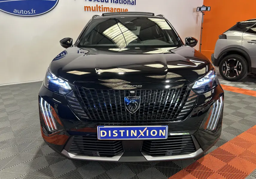 Vue frontale d'un Peugeot 2008 Hybrid 136 e-DCS6 GT noir avec phares LED et calandre imposante en intérieur showroom.