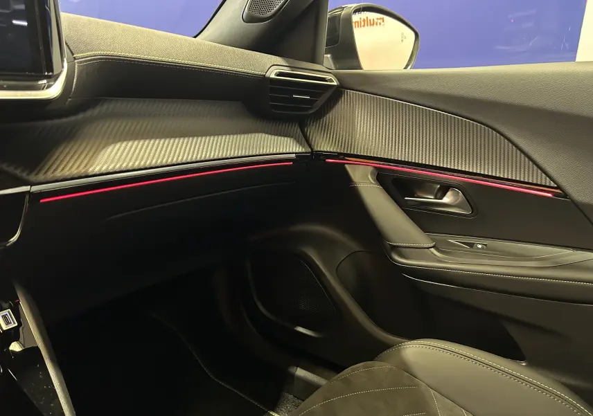Vue intérieure côté passager du Peugeot 2008 Hybrid 136 e-DCS6 GT noir avec éclairage d'ambiance rouge et finition carbone.