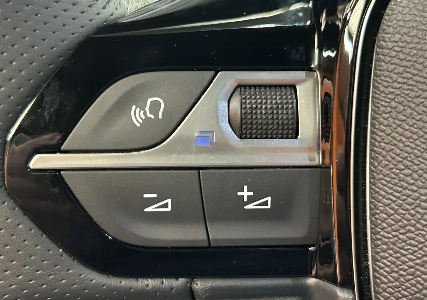 Gros plan sur les commandes du volant noir du Peugeot 2008 Hybrid 136 e-DCS6 GT, avec molette et boutons de réglage.