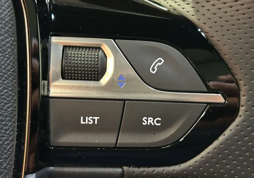 Gros plan sur les commandes noires et argentées du volant du Peugeot 2008 Hybrid 136 e-DCS6 GT, avec boutons LIST et SRC visibles.