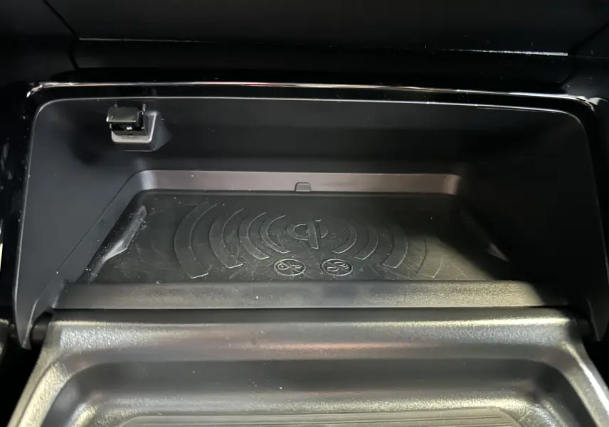 Gros plan sur le compartiment de recharge sans fil noir dans l'habitacle du Peugeot 2008 Hybrid 2025.