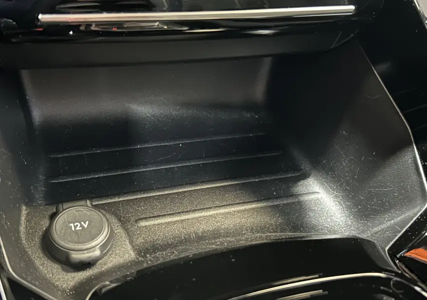 Gros plan sur la prise 12V et le rangement central noir intérieur du Peugeot 2008 Hybrid 136 e-DCS6 GT.