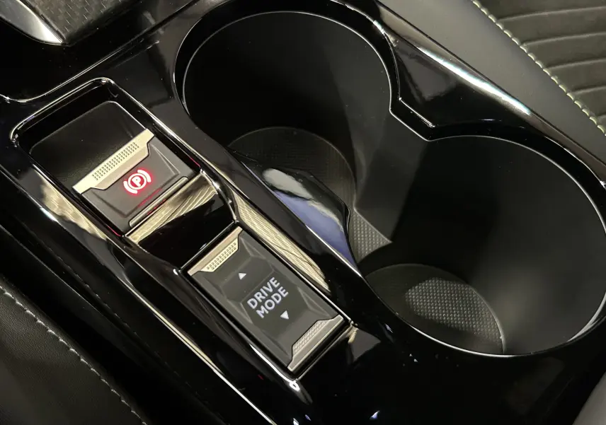 Gros plan sur la console centrale noire du Peugeot 2008 Hybrid 136 e-DCS6 GT avec boutons frein à main électrique et mode de conduite.