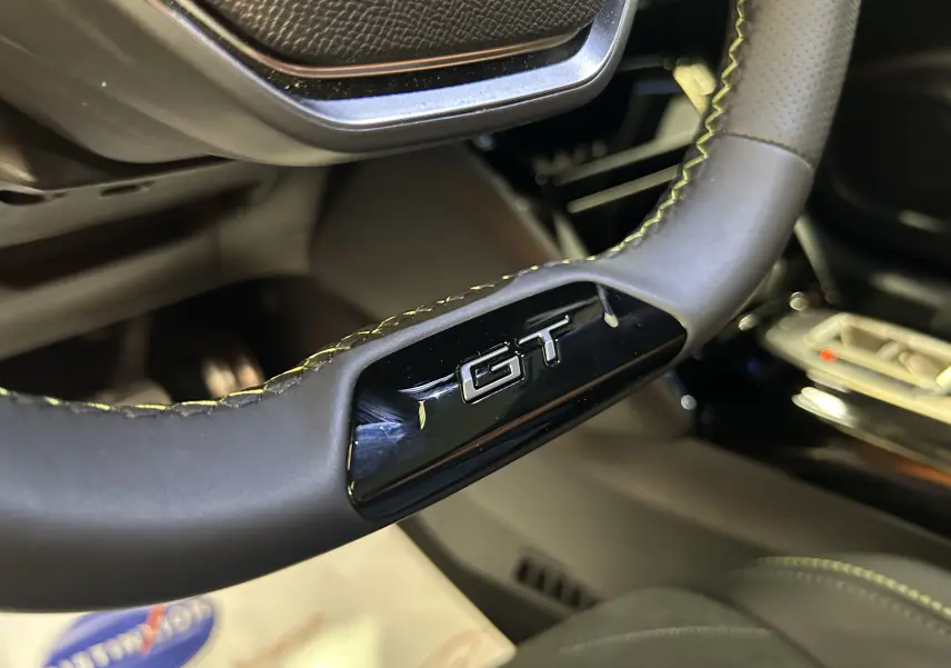 Gros plan sur le volant cuir noir avec logo GT du Peugeot 2008 Hybrid 136 e-DCS6 GT, intérieur moderne et soigné.