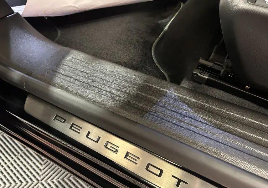 Gros plan sur la plaque de seuil de porte en métal avec logo Peugeot, intérieur noir du SUV 2008 Hybrid 2025.