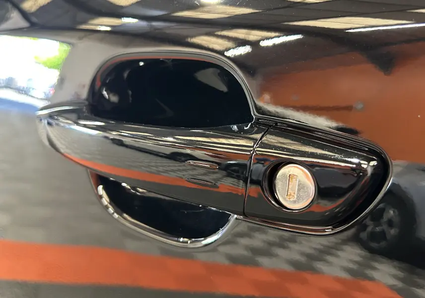Gros plan sur la poignée de porte noire brillante d'une Peugeot 2008 Hybrid 136 e-DCS6 GT, avec serrure visible.