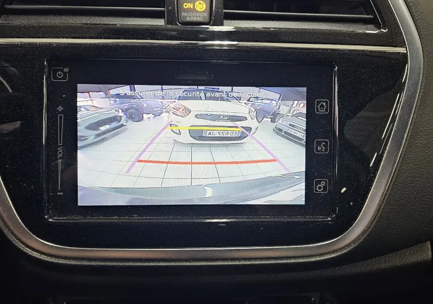 Écran central affichant la caméra de recul du Suzuki SX4 S-Cross 2020 avec vue arrière sur un véhicule blanc en intérieur.