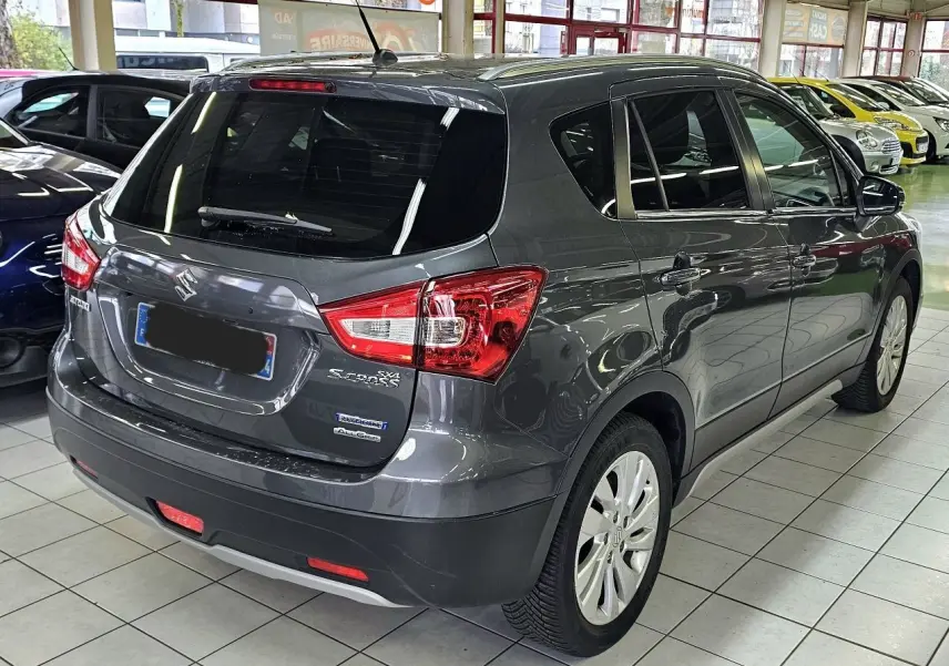 Vue 3/4 arrière droite d'un Suzuki SX4 S-Cross gris métallisé en showroom, avec badges Hybrid et AllGrip visibles.