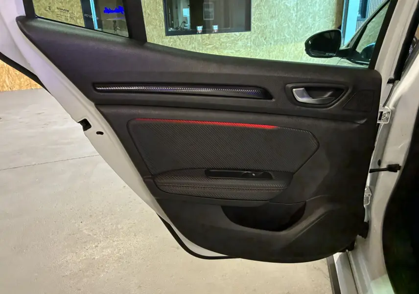 Vue intérieure côté gauche de la porte avant blanche d'une Renault Mégane IV RS 280 avec insert carbone et surpiqûre rouge.