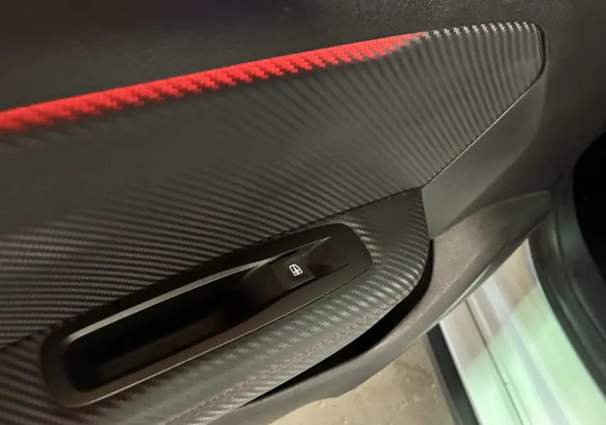 Gros plan sur la commande des vitres côté gauche de la porte intérieure noire avec insert carbone et surpiqûre rouge de la Renault Mégane IV RS 280 EDC6.