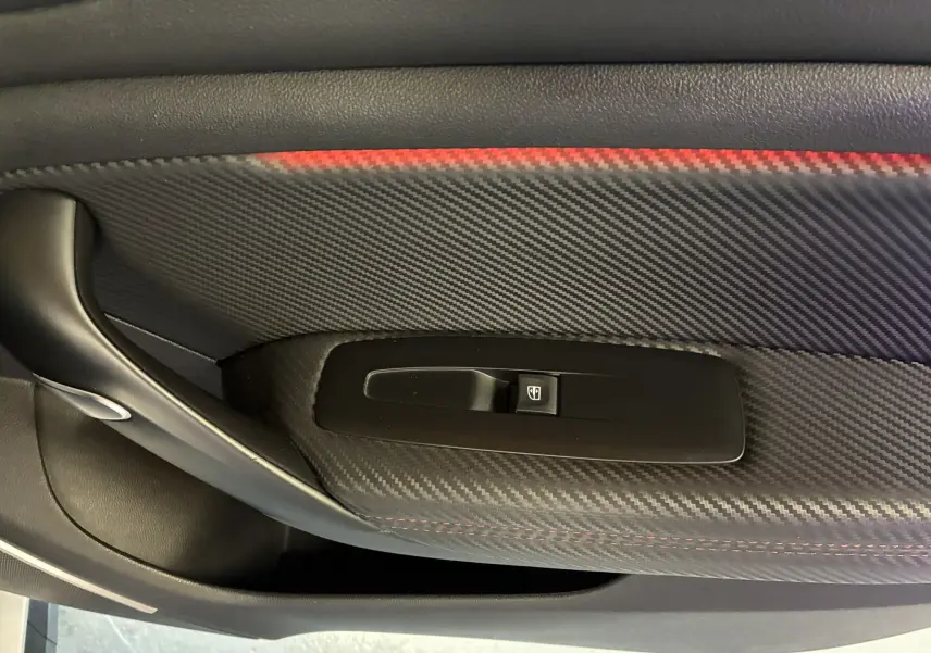 Gros plan sur la commande de lève-vitre côté porte intérieure en finition carbone avec surpiqûres rouges d'une Renault Mégane IV RS 280 blanche.