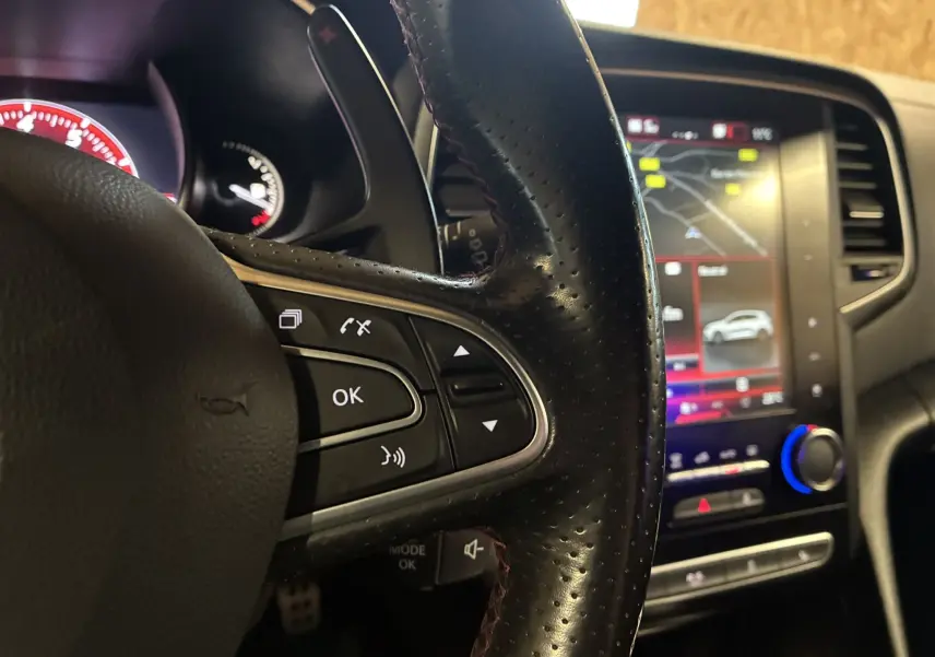 Vue intérieure côté conducteur de la Renault Mégane IV RS 280 EDC6 avec tableau de bord noir et écran tactile central allumé.