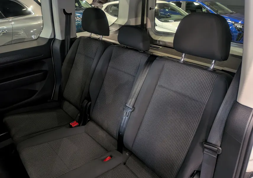 Vue intérieure sur la banquette arrière en tissu noir du Volkswagen Caddy 2025, avec ceintures de sécurité visibles.