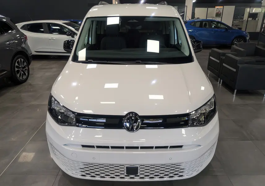 Vue avant d'un Volkswagen Caddy blanc 2025 exposé en showroom avec calandre noire et logo VW centré.