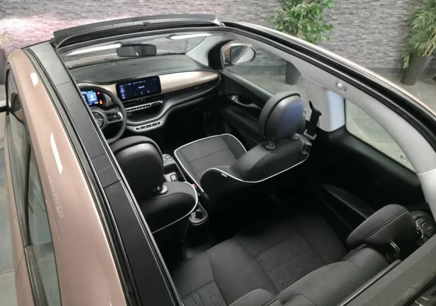 Vue intérieure plongeante de la FIAT 500 Cabriolet électrique rose, avec capote ouverte et sellerie noire contrastée.
