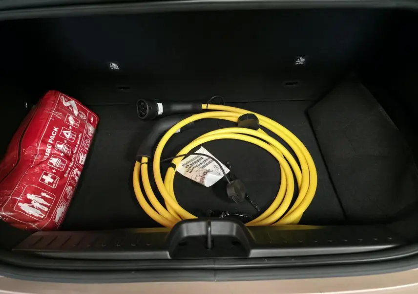 Vue plongeante sur le coffre d'une FIAT 500 Cabriolet électrique rose, avec câble de recharge jaune et trousse de secours rouge.