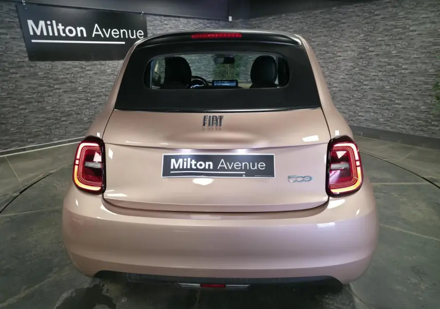 Vue arrière d'une FIAT 500 Cabriolet électrique rose métallisée avec capote noire et feux arrière LED allumés.