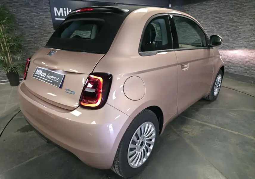 Vue 3/4 arrière droite d'une FIAT 500 Cabriolet électrique rose métallisé avec capote noire et feux LED distinctifs.