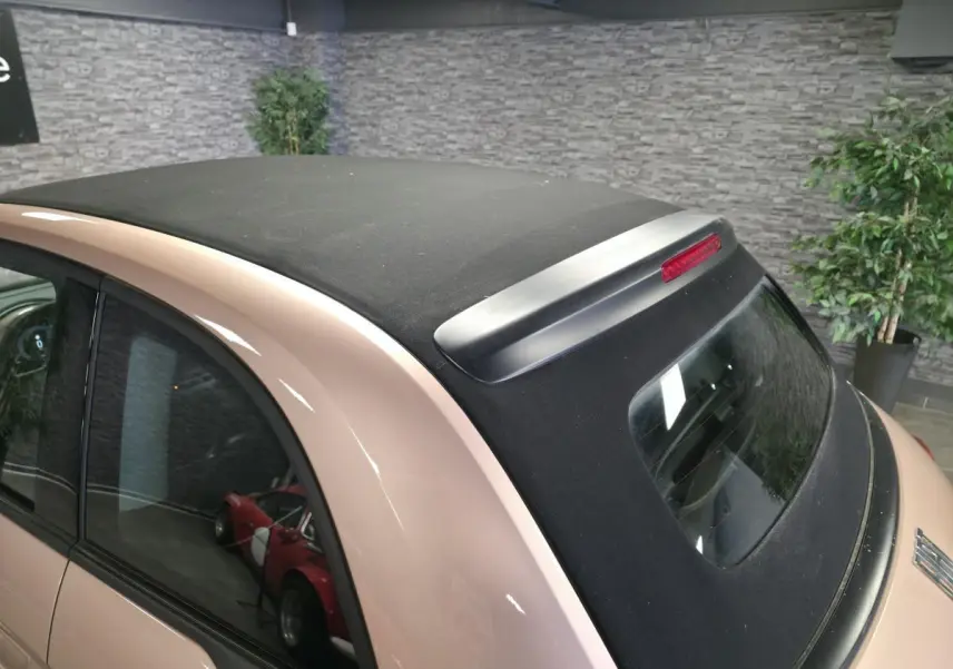Vue arrière 3/4 d'une FIAT 500 Cabriolet électrique rose avec capote noire et feu stop intégré sur le toit.